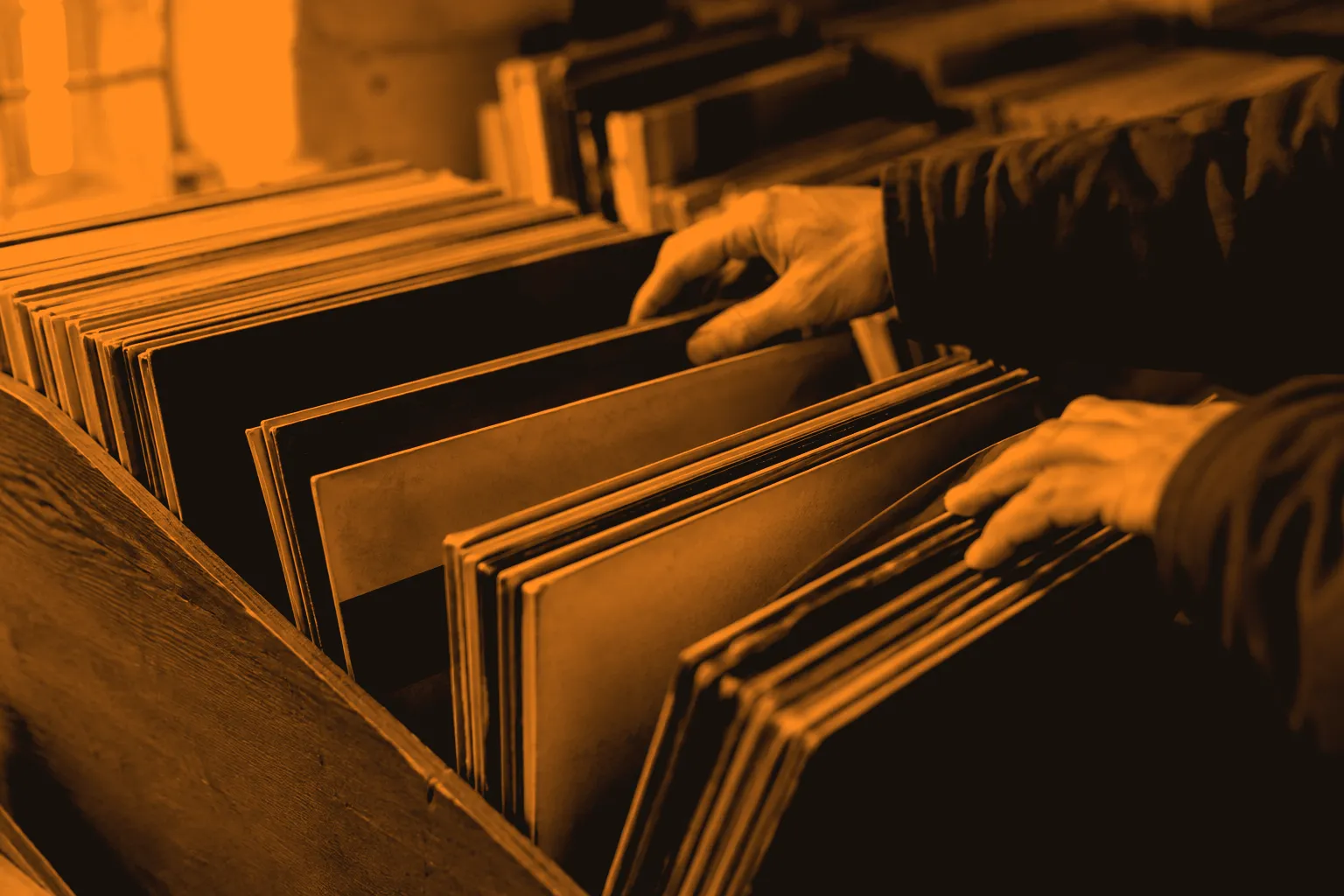 Hands browsing vinyl sleeves in a wooden record-shop crate.