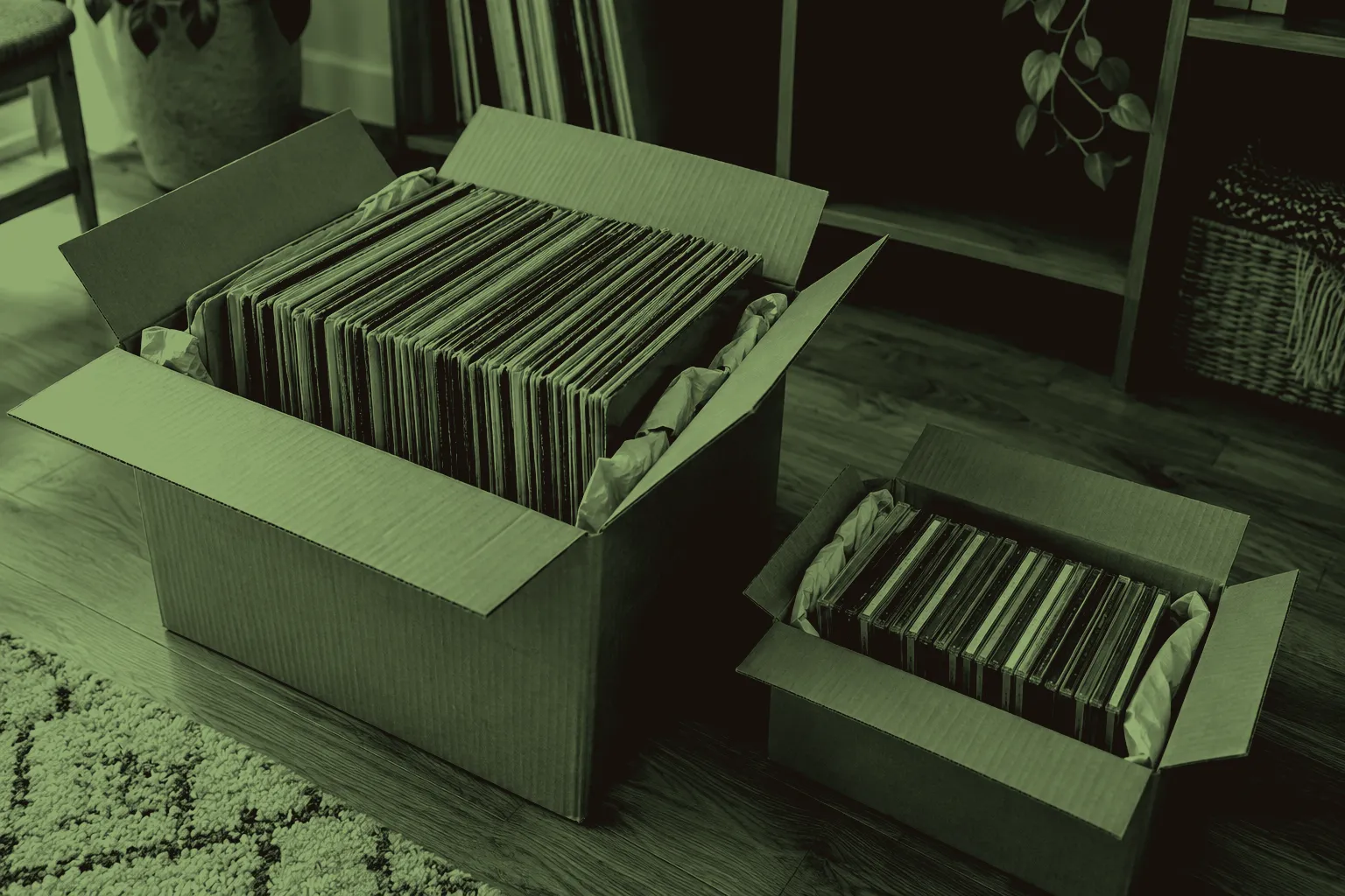 Records and CDs stand upright in separate cardboard moving boxes, cushioned with packing paper beside partly emptied shelves.