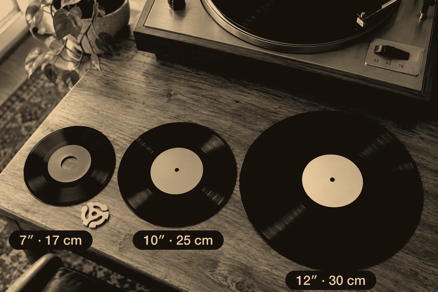 A 7-inch, a 10-inch and a 12-inch record side by side on a wooden table, with a yellow 45 adapter and a turntable speed switch for 33, 45 and 78.