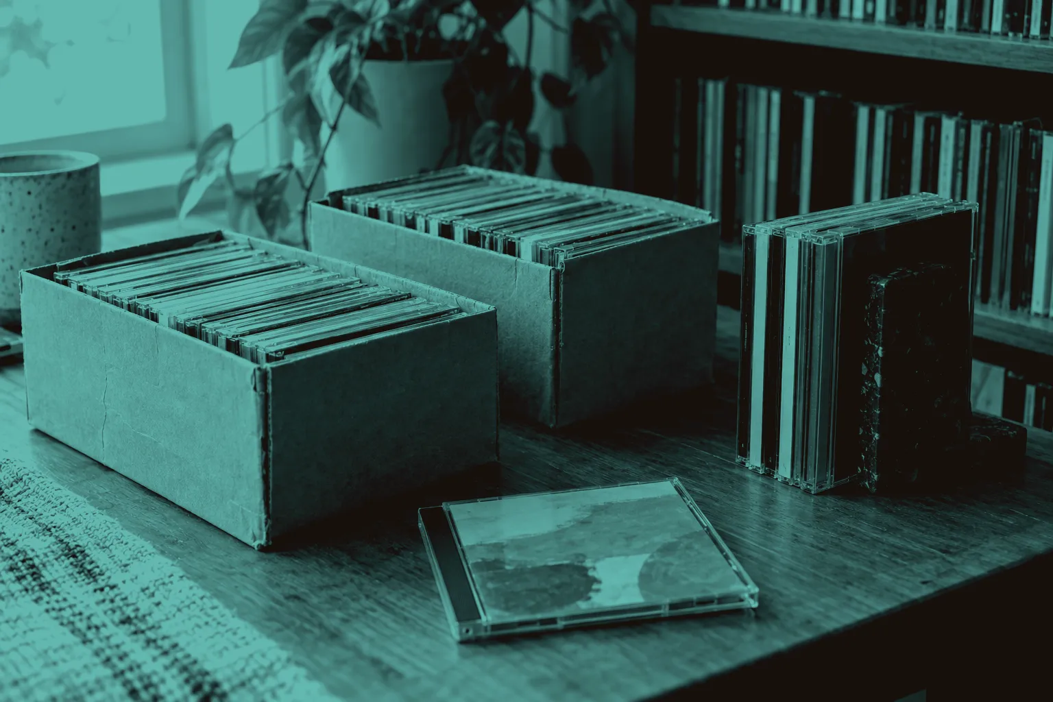 CD cases standing upright in two small cardboard boxes and beside a bookend on a wooden table.